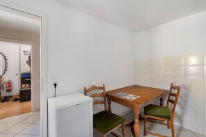 Une petite cuisine avec une table et des chaises en bois, un réfrigérateur blanc et un mur recouvert de carreaux.