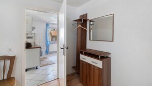 A room with a wooden wardrobe, a mirror, and a door leading to a kitchen area.