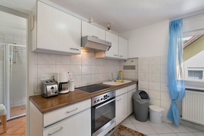 Een keuken met witte kasten, een houten aanrecht, een ingebouwde oven, een spoelbak en een prullenbak.