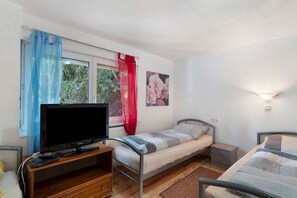 Une chambre à coucher comprenant un lit, une télévision, une table de chevet, une commode, une fenêtre avec des rideaux et un luminaire fixé au mur.