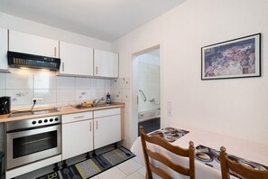Una cocina moderna con armarios blancos, horno empotrado, lavamanos y comedor con mesa y sillas.
