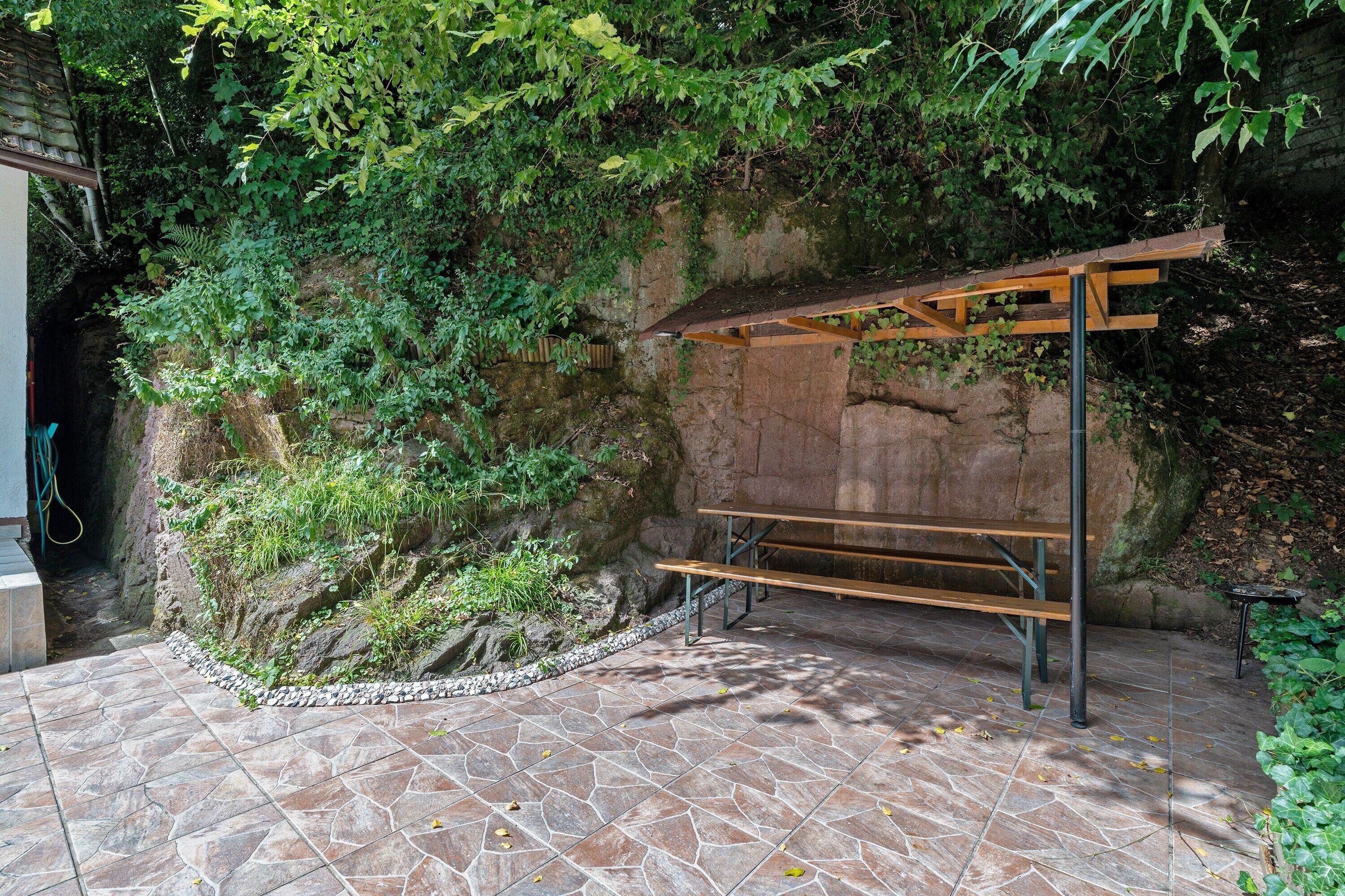 A stone-tiled patio with a wooden bench and a pergola structure.