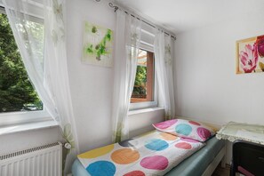 Un dormitorio con cama, ventana, radiador y una mesita.