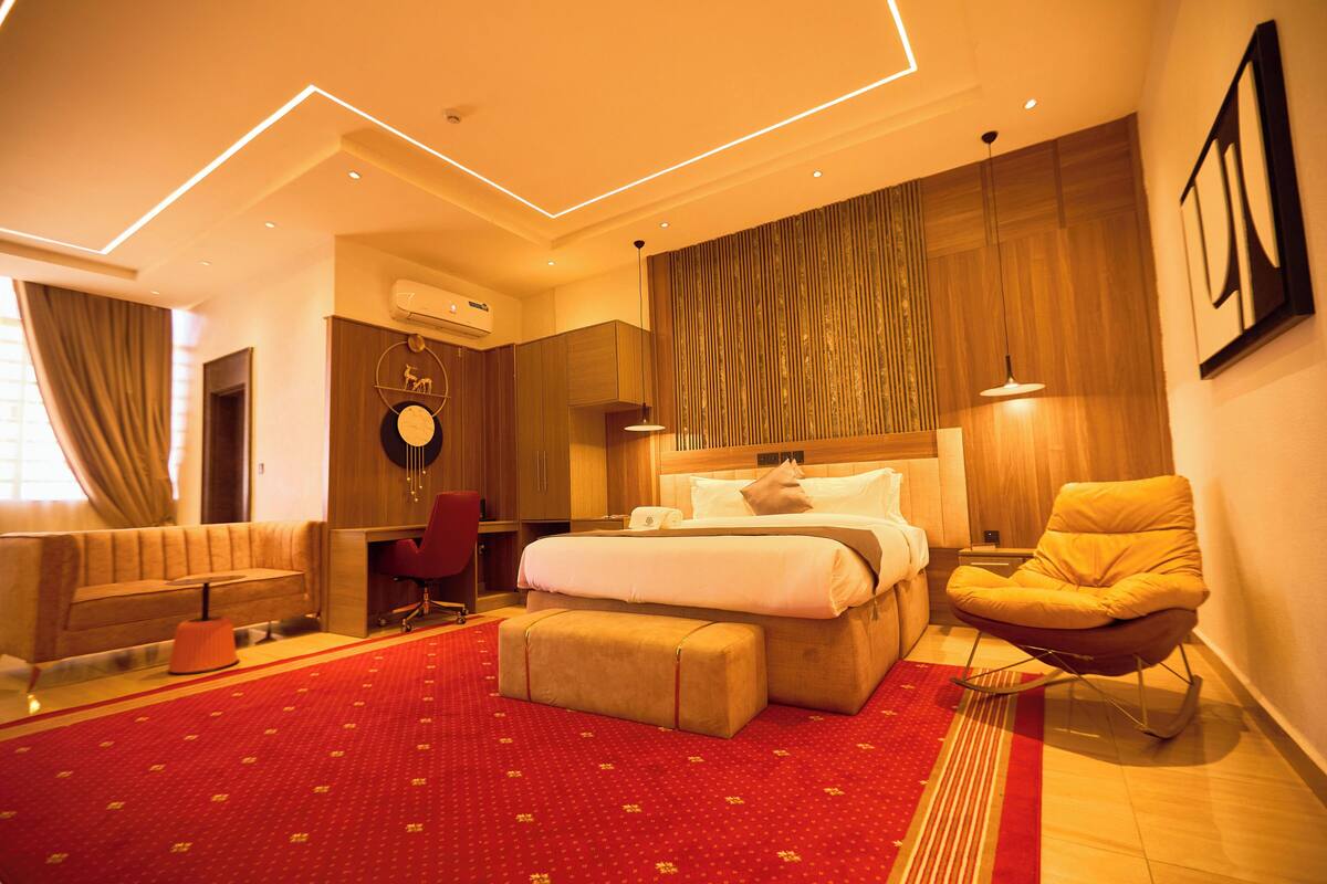 A modern hotel room with a large bed, a sofa, a red carpet, and a wooden accent wall.