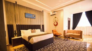 A modern hotel room with a large bed, a small table, a sofa, and a patterned rug. - Bourdillon Hotel & Apartments Airport Rd (Abuja)