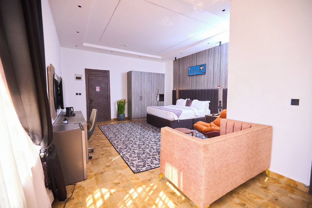 A modern hotel room with a bed, a sofa, a desk, and a television.