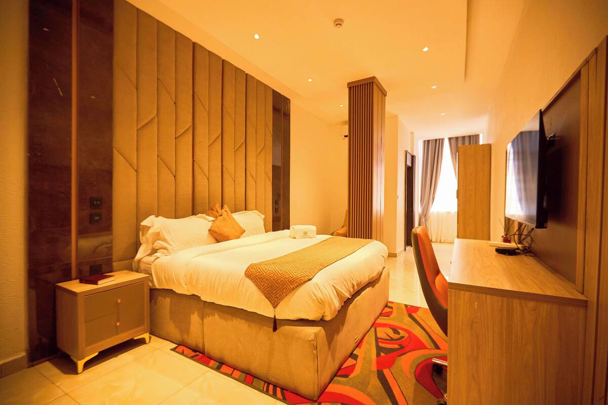 A modern hotel room with a large bed, a desk, a TV, and a wardrobe.