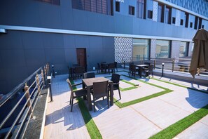 An outdoor seating area with tables and chairs, a patterned wall, and a building facade in the background. - Bourdillon Hotel & Apartments Airport Rd (Abuja)