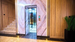 A marble wall with a glass elevator door, a wooden staircase, and a potted plant. - Bourdillon Hotel & Apartments Airport Rd (Abuja)