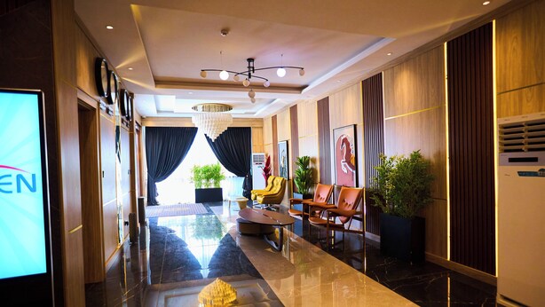 A hotel lobby with a marble floor, a chandelier, seating area, and a large screen displaying 'EN'. - Bourdillon Hotel & Apartments Airport Rd (Abuja)