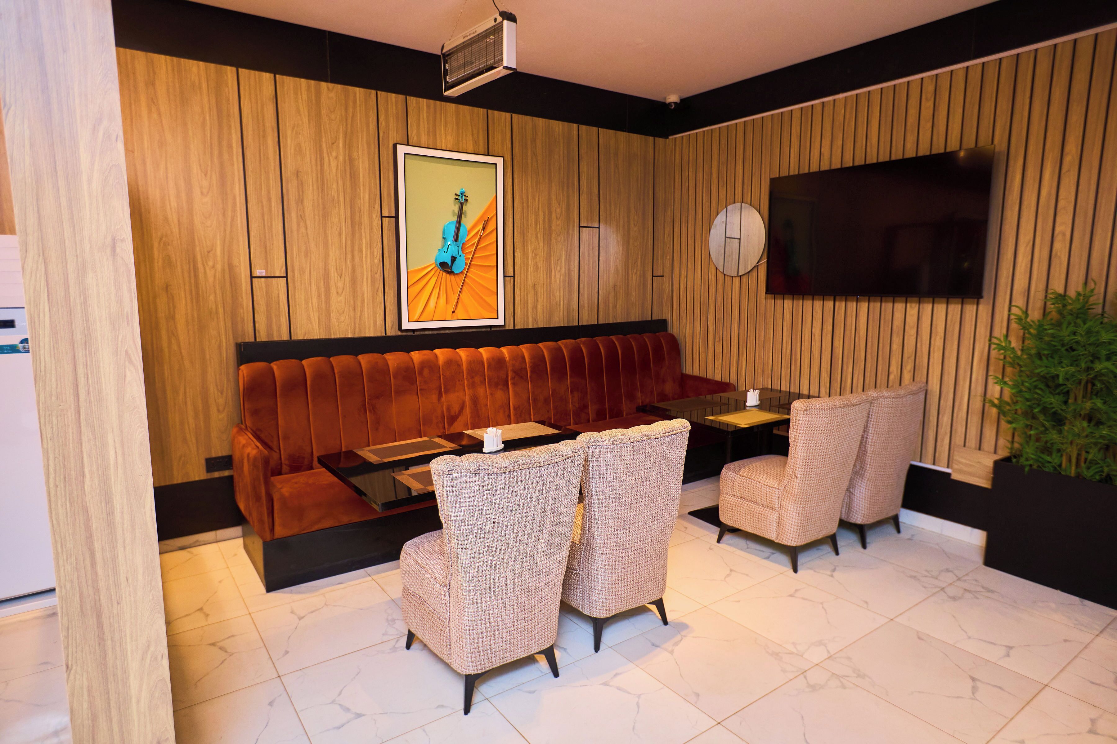 Un intérieur moderne avec un mur lambrissé en bois, un canapé, deux fauteuils, un téléviseur à écran plat et un projecteur fixé au plafond.