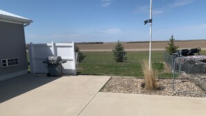 A backyard with a grill, a white fence, a flagpole, and a chain-link fence with chairs. - Lake Oahe Retreat (Pierre)