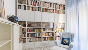 Ein Zimmer mit einem großen Bücherregal voller Bücher, einem gemusterten Sessel mit Zierkissen und einem Marmorboden.