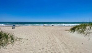 A sandy beach with a clear blue sky, a trash bin, and sparse vegetation. - Bogue Shores Ground floor Studio condo-queen bed, 3 min walk to beach, near pool (Atlantic Beach)