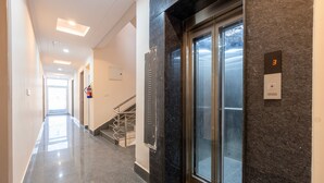A modern hallway with a glass elevator, a fire extinguisher, and a staircase. - Hotel park Tree I Sec-63a I Noida (Noida)