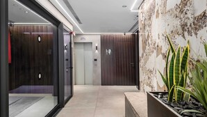 Een moderne lobby met een glazen lift, een receptiebalie en een plant.