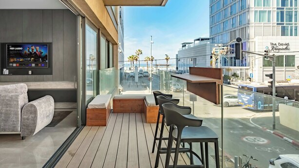 Een modern balkon met een bank, houten zitplaatsen en een televisiescherm.