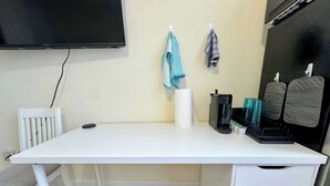 Un escritorio blanco con una silla, una máquina de café negra, un rollo de toallas de papel y un juego de tazas.