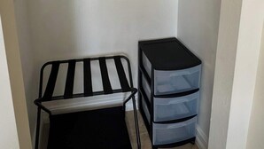 Un armario pequeño con una repisa metálica, una silla negra y un mueble de almacenamiento azul.