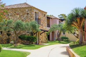 A stone building with a tiled roof, a paved pathway, and surrounding greenery. - Valtur Sardegna - Eos Costa Rei  (Costa Rei)