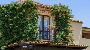 A house with a covered porch, stone columns, and a balcony with red flowers. - Valtur Sardegna - Eos Costa Rei  (Costa Rei)