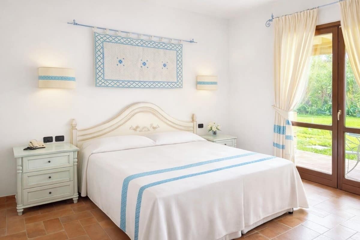 A bedroom with a bed, nightstands, a wall-mounted light, and a window with curtains.