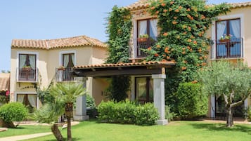 A building with a tiled roof, a covered patio, and a garden with palm trees and shrubs.