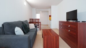 A modern living room with a grey sofa, wooden coffee table, and a TV on a wooden cabinet. - Charming Apart for 4 Near the Sea (Agde)