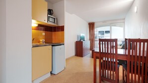 A compact kitchen with a microwave, refrigerator, and a dining area with wooden chairs and a table. - Charming Apart for 4 Near the Sea (Agde)