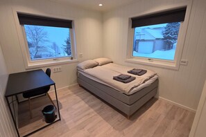 A small, modern bedroom with a single bed, a desk, and two windows. - Arctic Nine - Sentralt hus på øya (Tromsø)