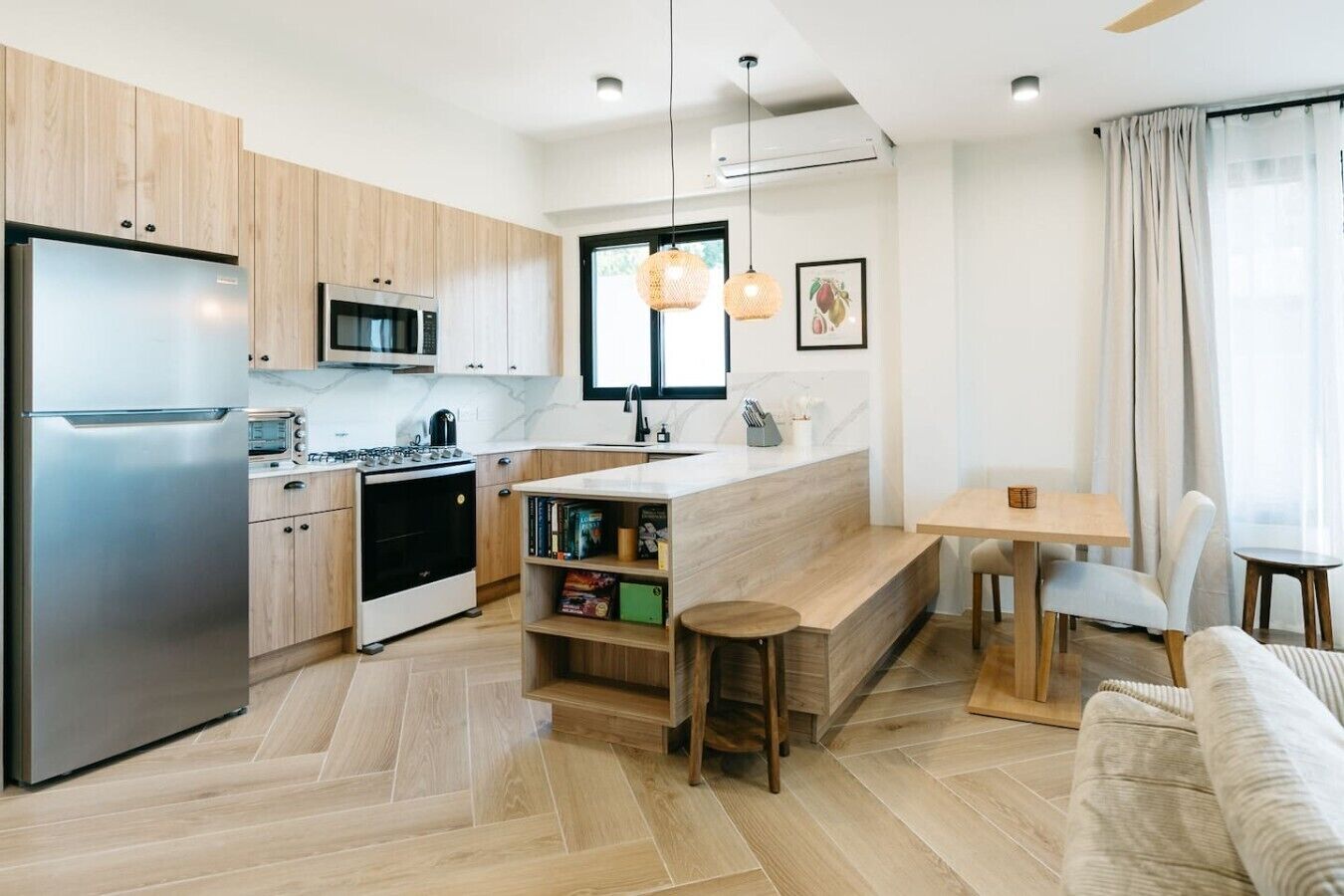 A modern kitchen with a built-in oven, microwave, and refrigerator. There is a dining area with a table and chairs, and a small seating area with a bench.