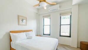 A bedroom with a bed, a ceiling fan, an air conditioning unit, and two windows. - Cinnamon Suite, Stylish 2BR | Central St George (Saint George's)