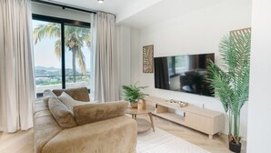 A modern living room with a large flat-screen TV, a beige sofa, a coffee table, and a potted plant. - Cinnamon Suite, Stylish 2BR | Central St George (Saint George's)