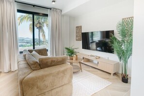 Un salon moderne avec un grand téléviseur à écran plat, un canapé beige, une table basse et une plante en pot.