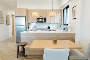 A modern kitchen with wooden cabinets, a built-in microwave, a toaster, and a large island with a sink. There are two pendant lights hanging above the island.