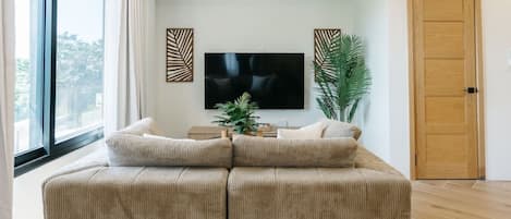 A living room with a large sectional sofa, a flat-screen TV, decorative wall art, a potted plant, and a wooden door.
