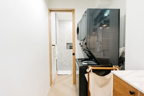 Une salle de bain moderne avec un grand miroir, un lavabo noir et une porte en bois donnant sur une autre pièce.