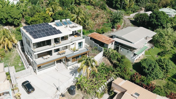 A modern two-story house with solar panels on the roof, a balcony, and a car parked in the driveway.