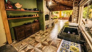 A kitchen with a brick oven, shelves with cookware, and a patterned floor. - Pesqueiro - rancho com lazer completo em Coxim/MS (Coxim)