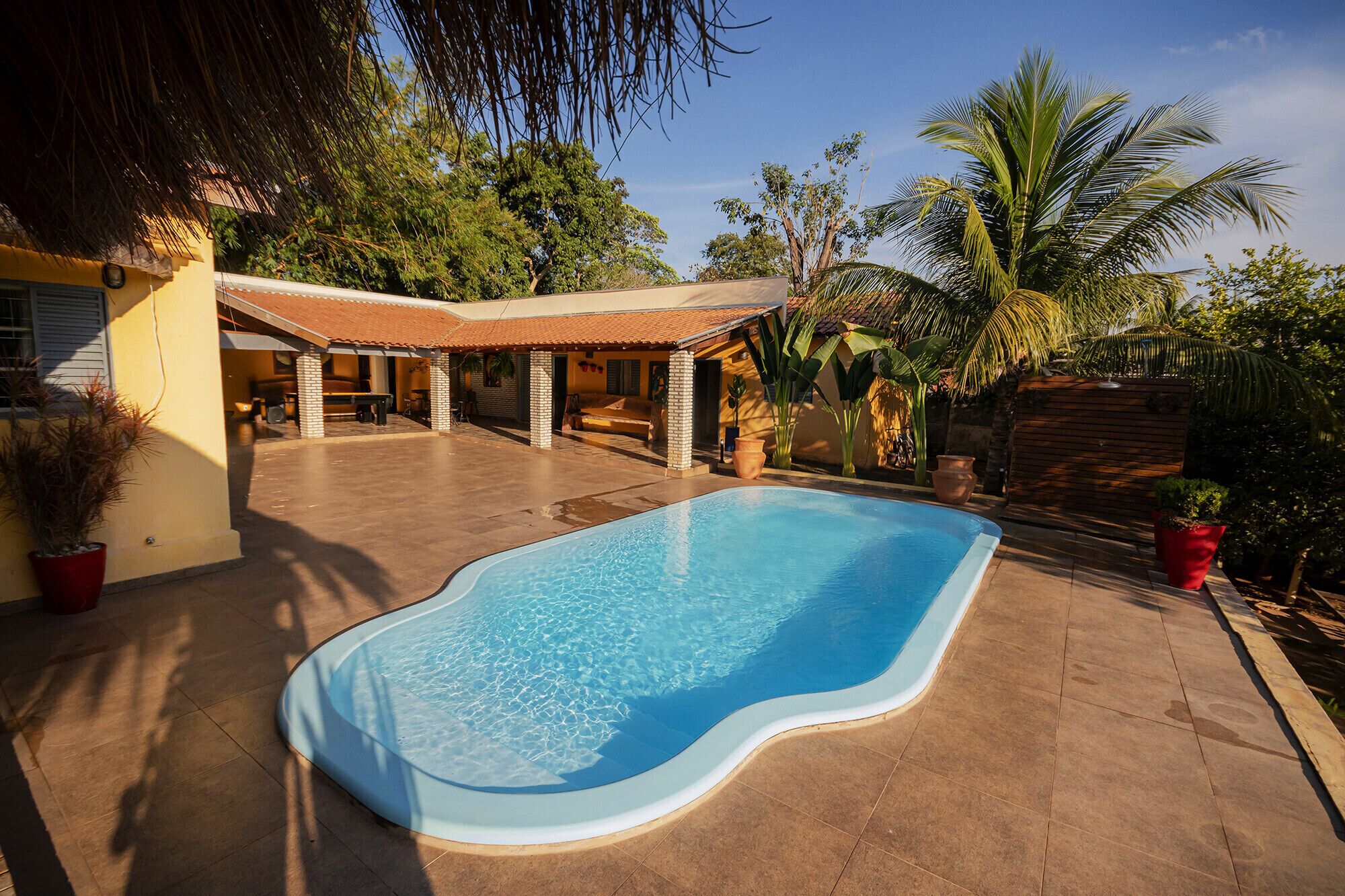 A swimming pool with a curved edge, surrounded by a patio area with a tiled floor and a covered seating area.