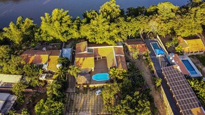 An aerial view of a residential area with houses, a swimming pool, and a river. - Pesqueiro - rancho com lazer completo em Coxim/MS (Coxim)