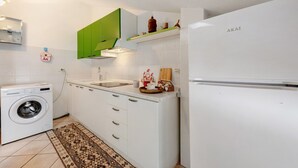 A compact kitchen with a washing machine, a sink, a refrigerator, and a green cabinet.