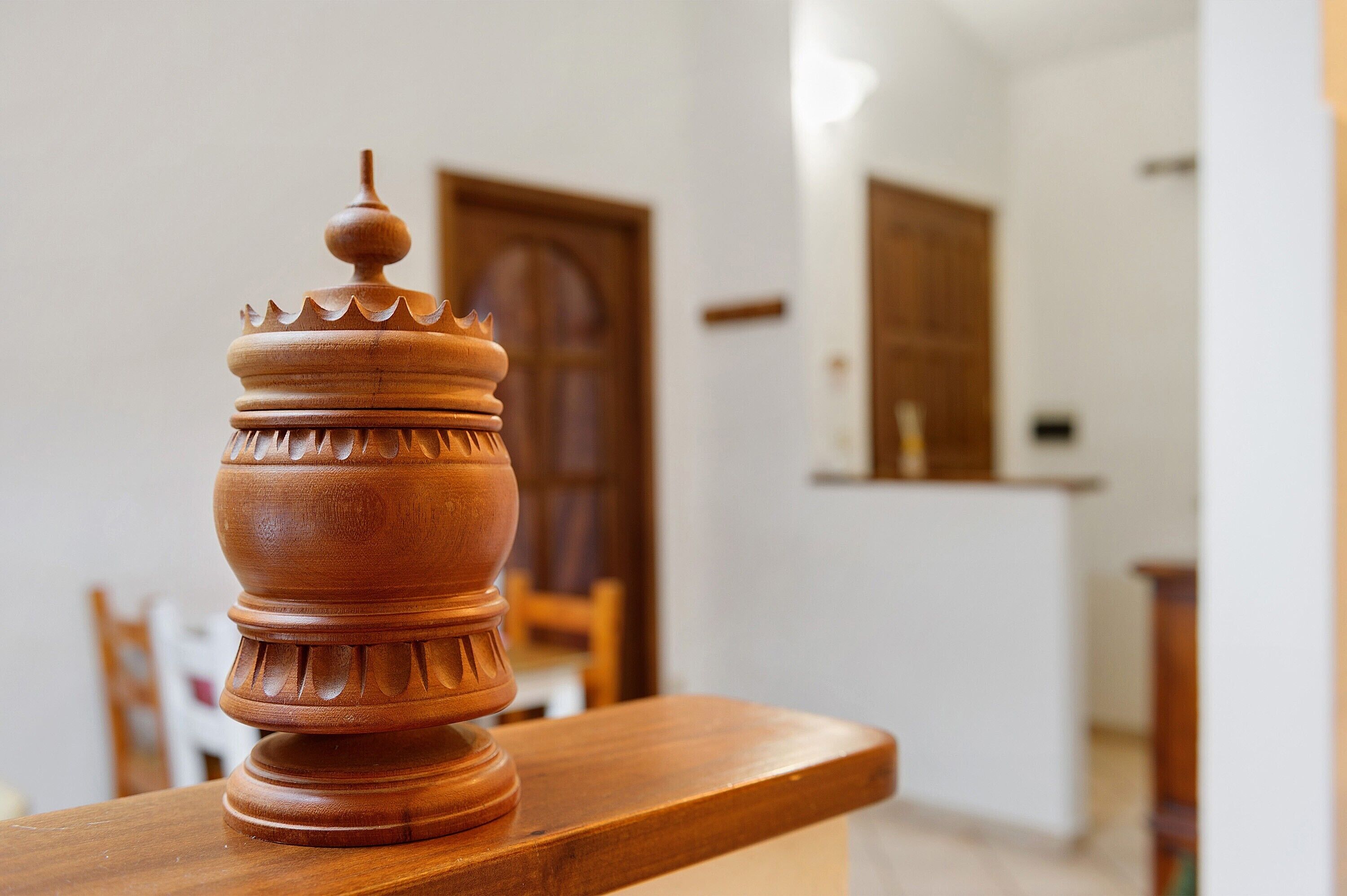 Una mesa de madera con un jarro decorativo encima, una puerta de madera y una pared blanca al fondo.