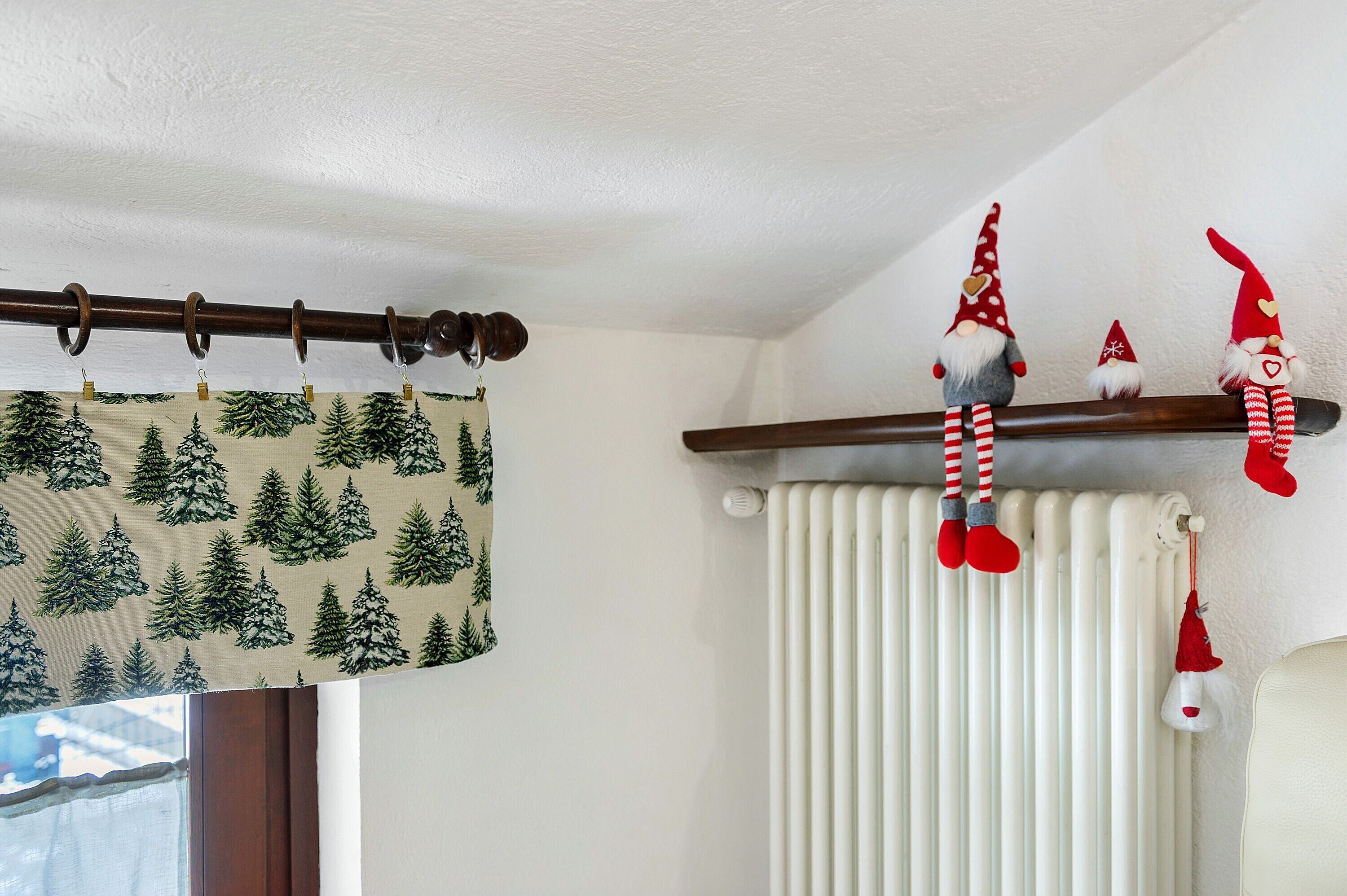 Une pièce avec un radiateur, un rideau orné d’un motif de forêt et une étagère décorée pour Noël.