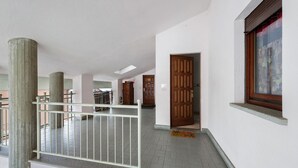A corridor with a white railing, wooden doors, and a window with a wooden frame.