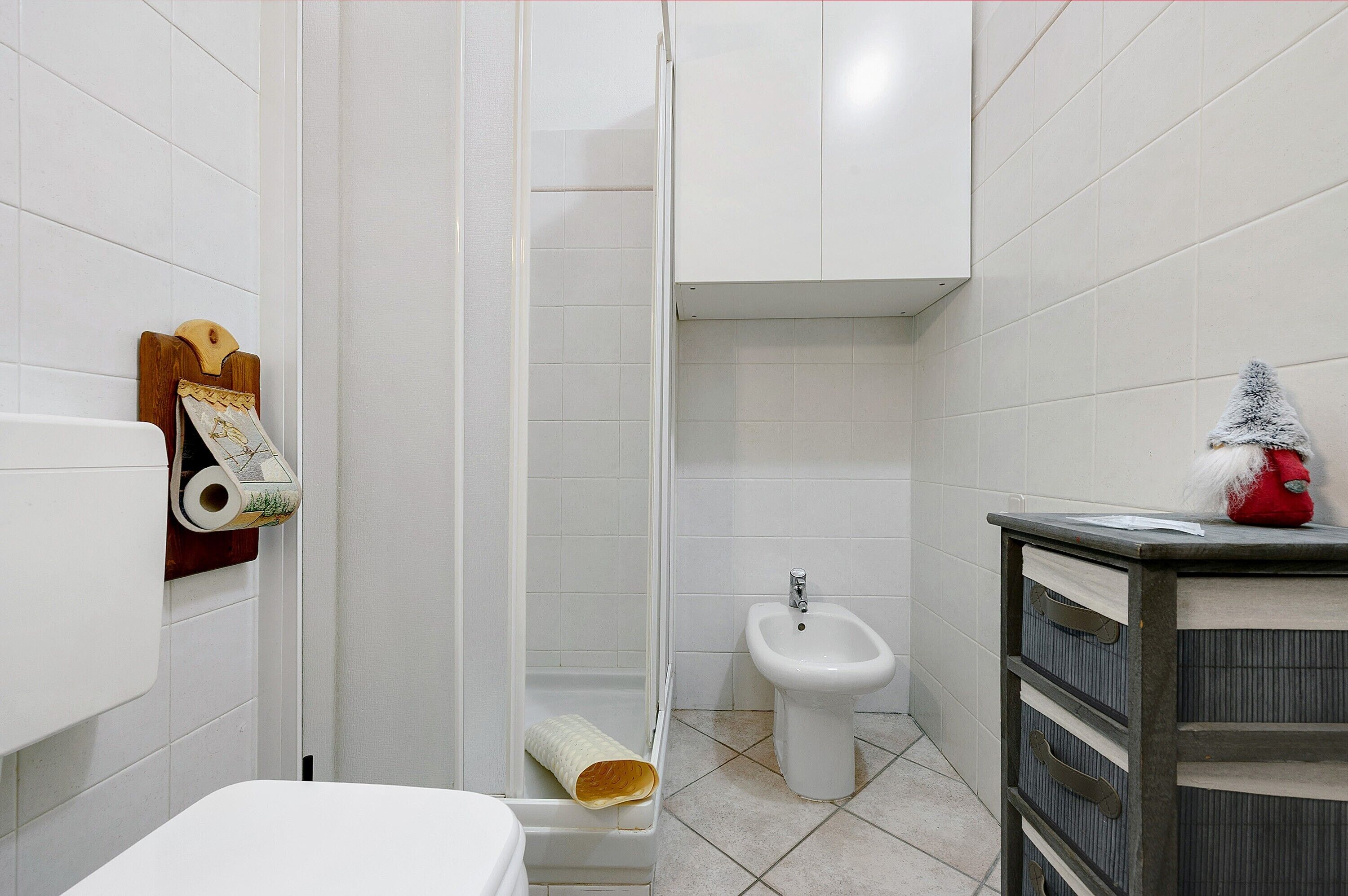 Een badkamer met een douche, toilet, bidet en een kast met lades.