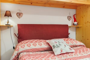 A bed with a red headboard, heart-patterned bedding, a lamp, and heart-shaped wall decorations.
