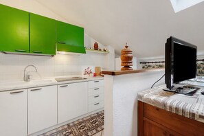 A kitchen with white cabinets, a green accent wall, a built-in stove, and a flat-screen TV on a wooden counter.