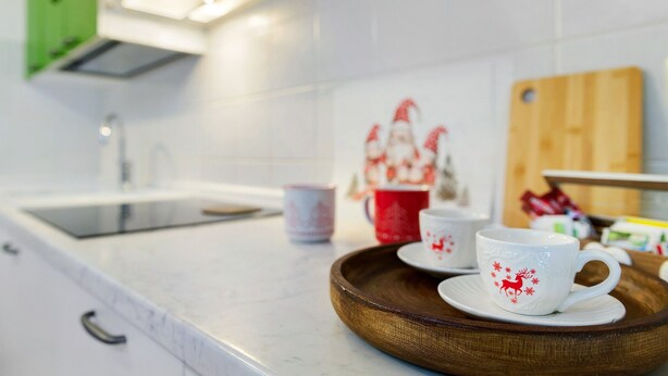 A kitchen counter with a tray holding two white cups with red designs, a red cup, and a wooden cutting board.