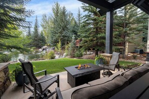 A patio with outdoor seating, a fire pit, and a view of a pond and trees.